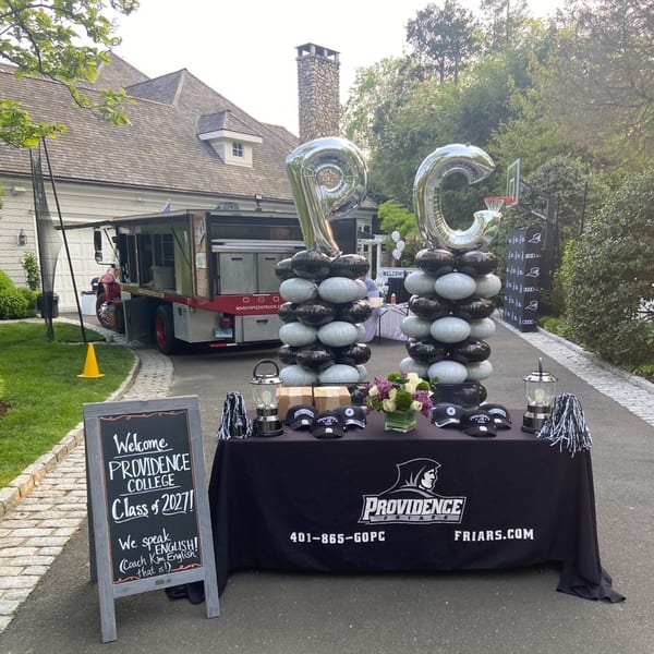 Marco Pizzeria food truck parked next to a Providence College welcome table with balloons and merchandise.