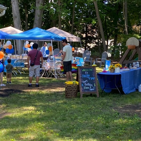 Outdoor birthday party with blue and orange balloons, tents, and a "Party Time" sign.