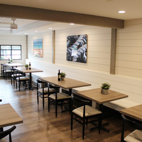 Interior of Marco Pizzeria with light wood tables, black chairs, and white shiplap walls with art.