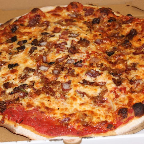 A close-up of a Marco Pizzeria pizza with melted cheese, bacon, and caramelized onions.