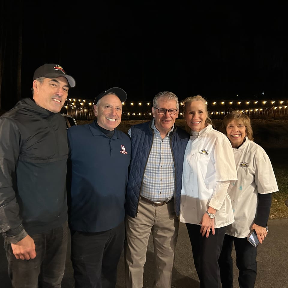 Five smiling people, including two women in Marco Pizza Truck chef coats, stand together at night.