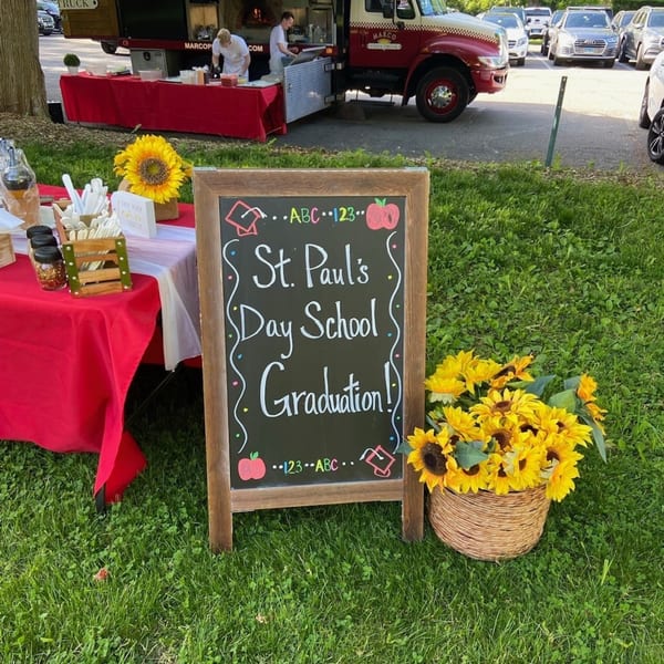 A Marco Pizzeria food truck, a red-draped table with condiments, and a "St. Paul's Day School Graduation!" sign.
