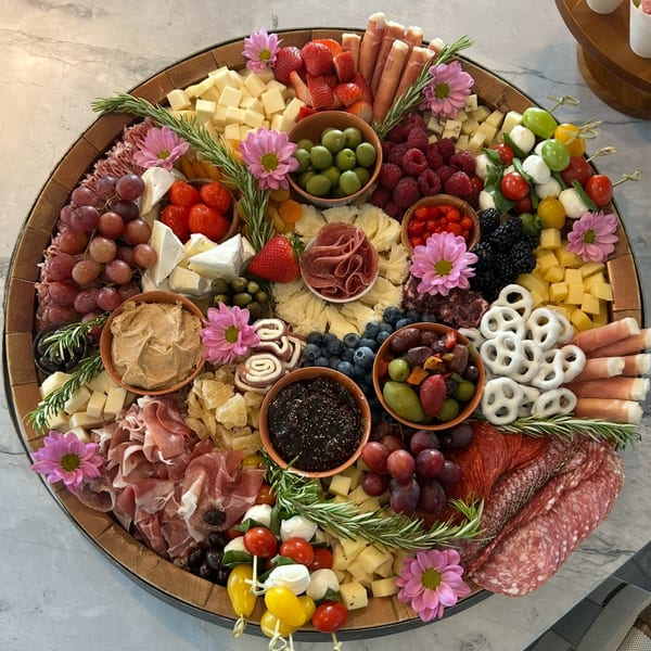 A large, round charcuterie board overflowing with Italian meats, cheeses, fruits, olives, and pretzels.