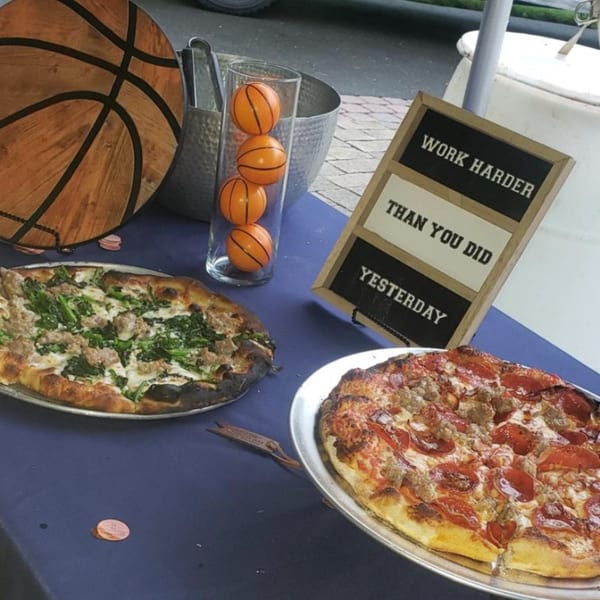 Two pizzas, one with sausage and greens, the other with pepperoni and sausage, on a blue table.