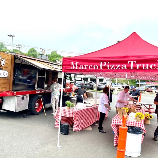Marco Pizza Truck and red tent with checkered tables and people serving food outdoors.