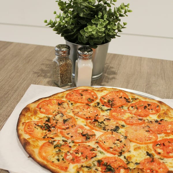 A Marco Pizzeria Margherita pizza with sliced tomatoes and basil, next to salt and pepper shakers.