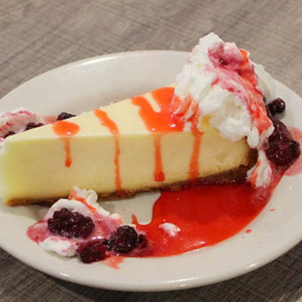 A slice of cheesecake with red berry sauce, whipped cream, and berries on a white plate.