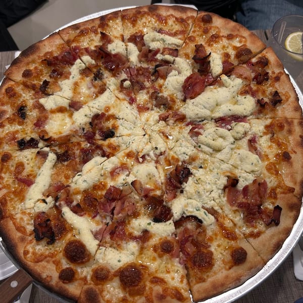 A whole Marco Pizzeria pizza, topped with ricotta cheese and bacon, sliced and ready to eat.