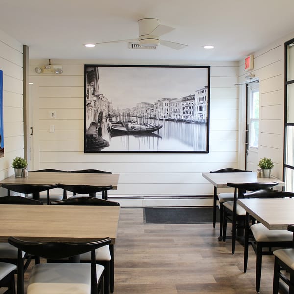 Marco Pizzeria's dining room with light wood tables, black chairs, and a large Venice canal mural.