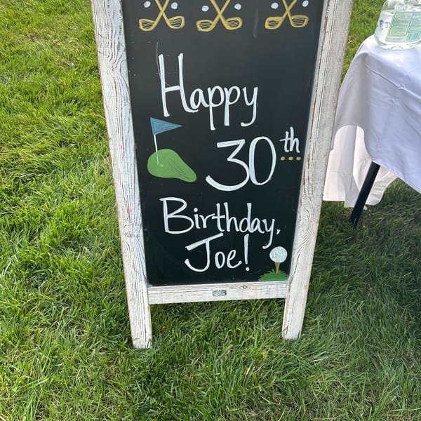 Chalkboard sign on grass reads "Happy 30th Birthday, Joe!" with golf-themed decorations.