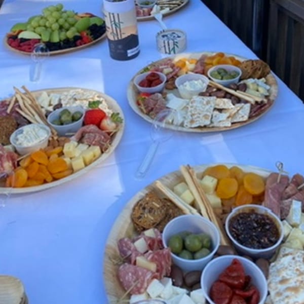 Three charcuterie boards with meats, cheeses, olives, crackers, and dried fruit on a white tablecloth.