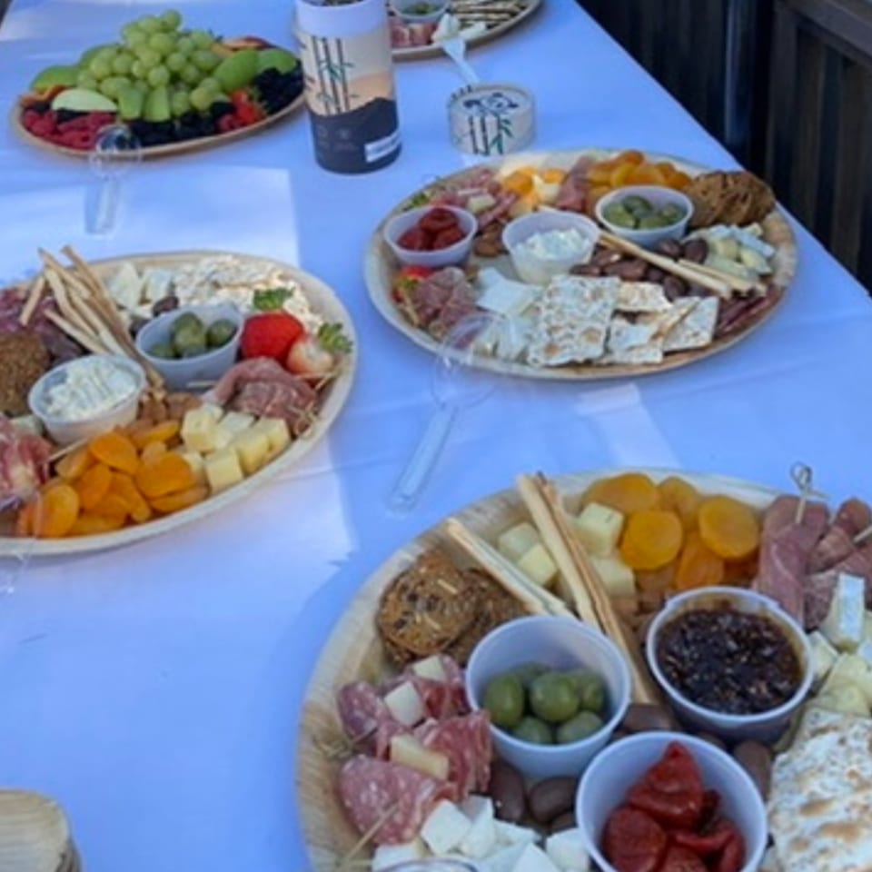 Three charcuterie boards with meats, cheeses, olives, crackers, and dried fruit on a white tablecloth.