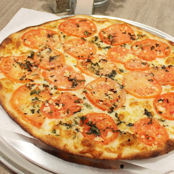 A freshly baked Marco Pizzeria Margherita pizza, topped with sliced tomatoes, mozzarella, and basil.