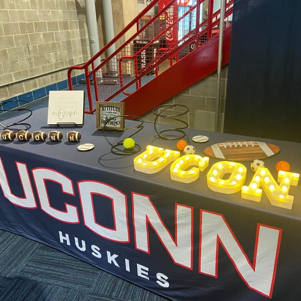 Table with UConn Huskies banner, light-up letters, mini footballs, and inspirational signs.