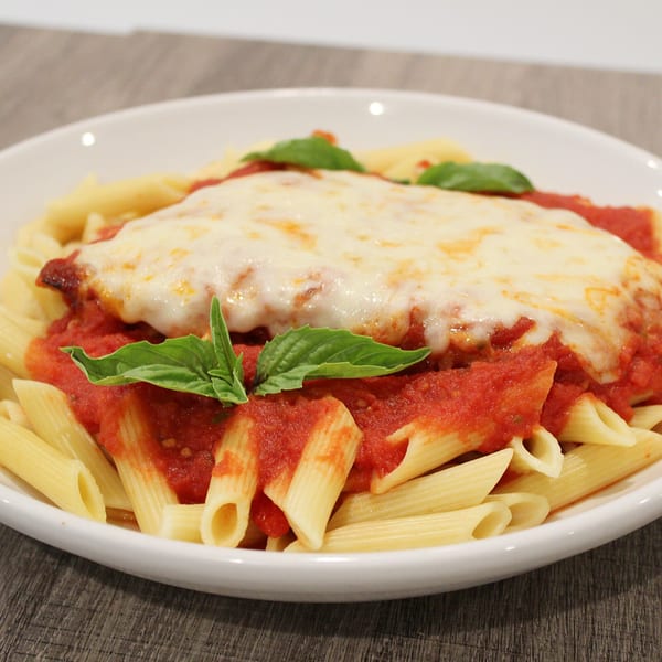 Chicken Parmesan with penne pasta, marinara sauce, melted cheese, and fresh basil in a white bowl.
