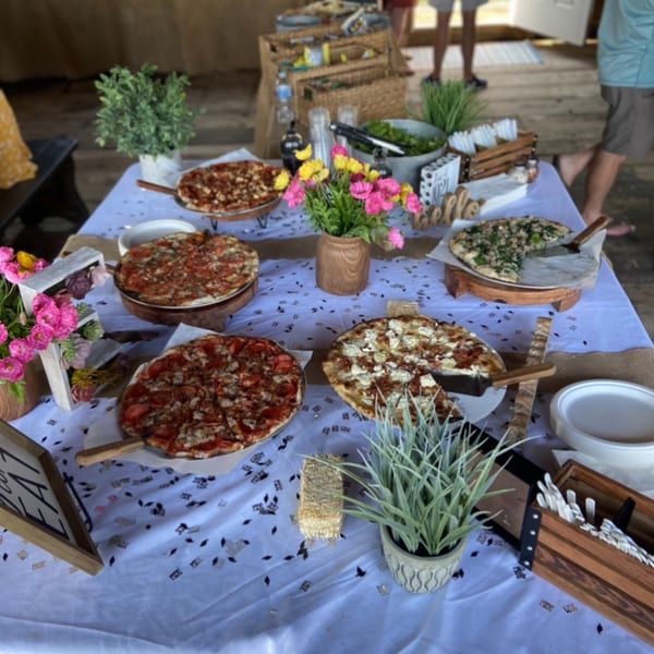A buffet table with five Marco Pizzeria pizzas, a salad bowl, and floral decorations.