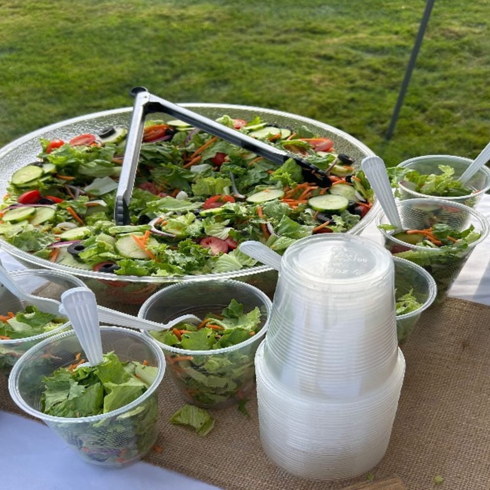Large bowl of garden salad with individual plastic cups of salad and a stack of empty cups.