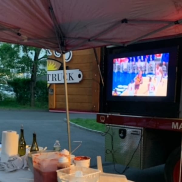 Outdoor setup with a TV showing a basketball game, food prep items, and a "TRUCK" sign.