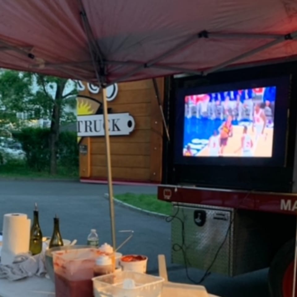 Outdoor setup with a TV showing a basketball game, food prep items, and a "TRUCK" sign.