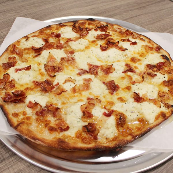 A white pizza with ricotta cheese and crispy bacon on a metal tray at Marco Pizzeria.